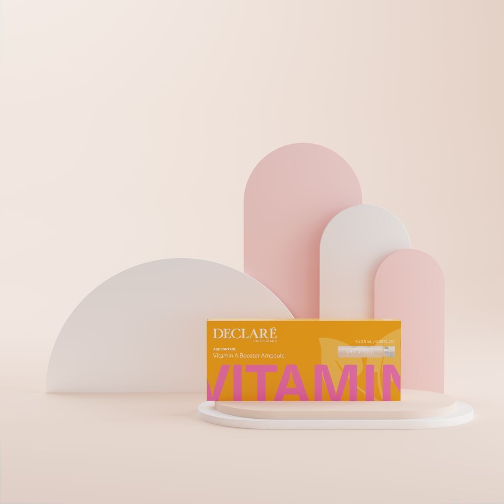 Gelbe Schachtel DECLARÉ Vitamin A Booster Ampulle auf Podest. Rosa Schriftzug "VITAMIN". Hintergrund mit Formen.