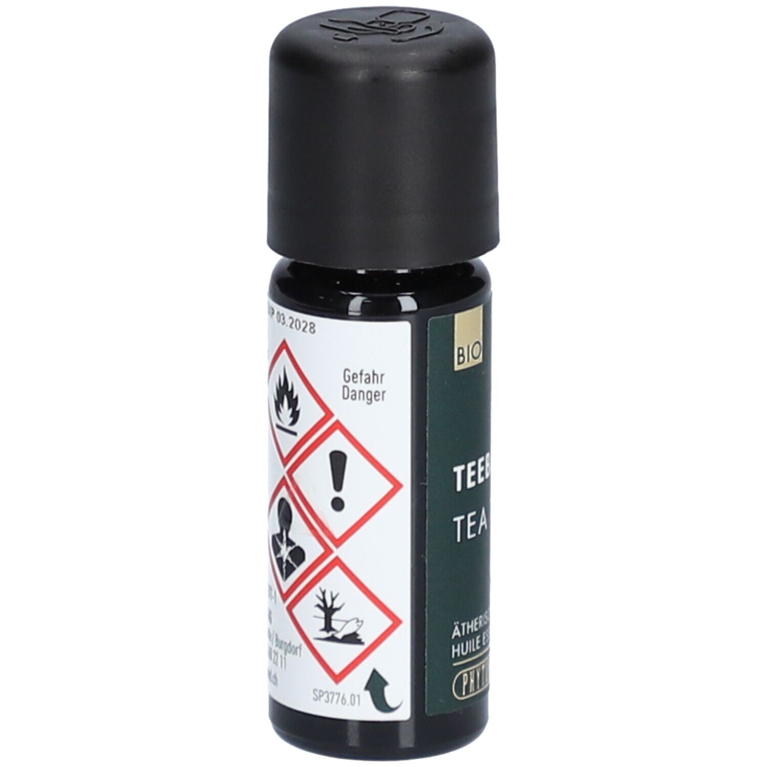 Flacon en verre brun avec bouchon noir. Symboles de danger et inscription : Tea Tree, huile essentielle. Marque : PHYTOMED.