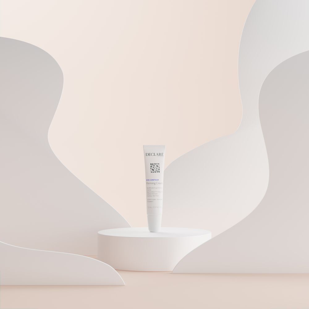 Weiße Tube DECLARÉ Eye Contour Firming Cream auf weißem Podest. Hintergrund mit weißen Formen.