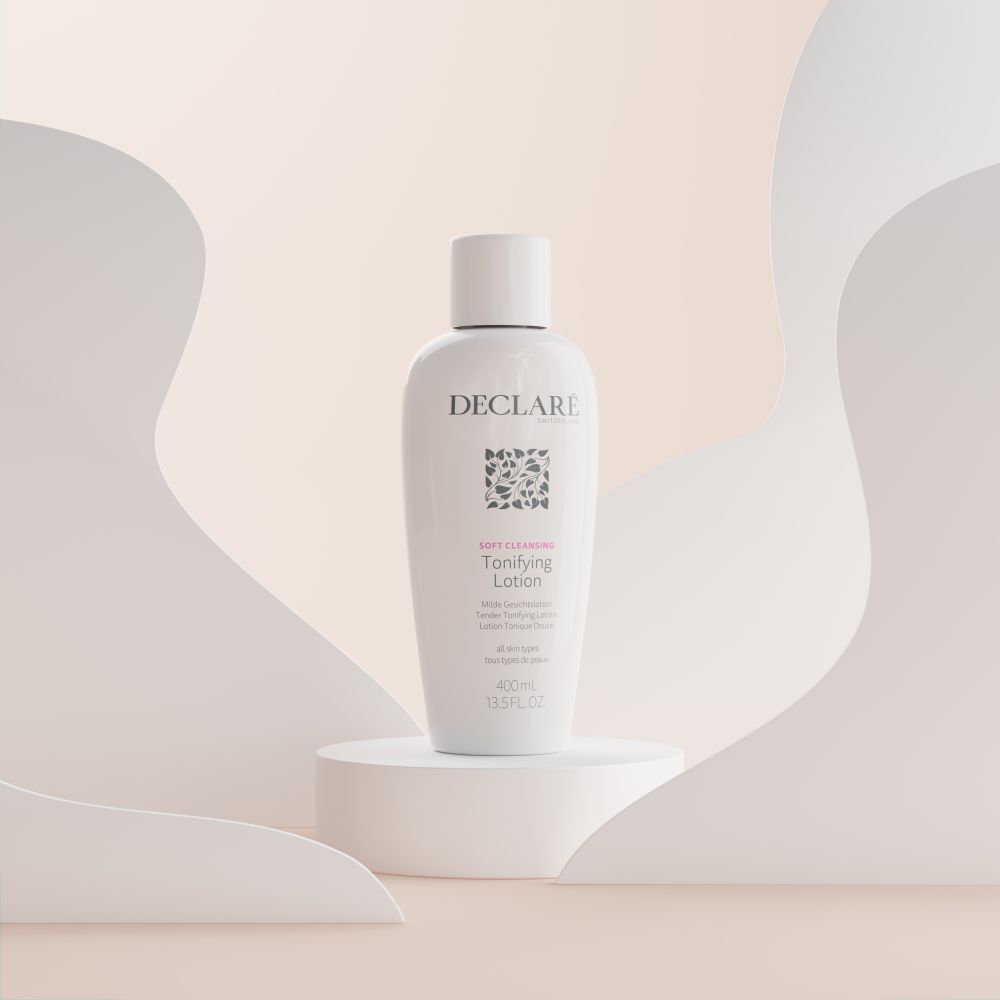 Weiße Flasche mit Deckel auf einem Podest. Aufschrift: DECLARÉ, Logo, Toning Lotion. Hintergrund mit weißen und beigen Formen.