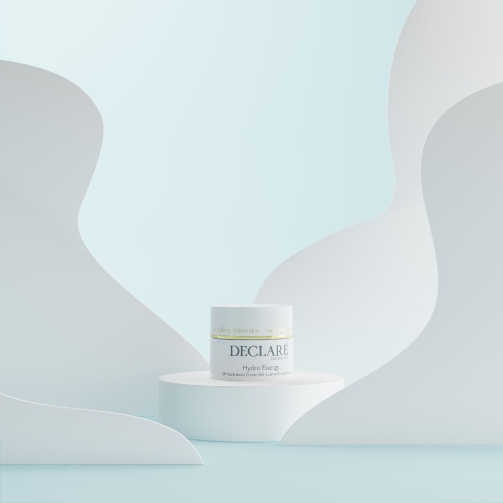 Weißer Tiegel auf einem Podest. DECLARÉ Hydro.Energy. Hintergrund mit weißen, geschwungenen Formen und blauem Farbverlauf.