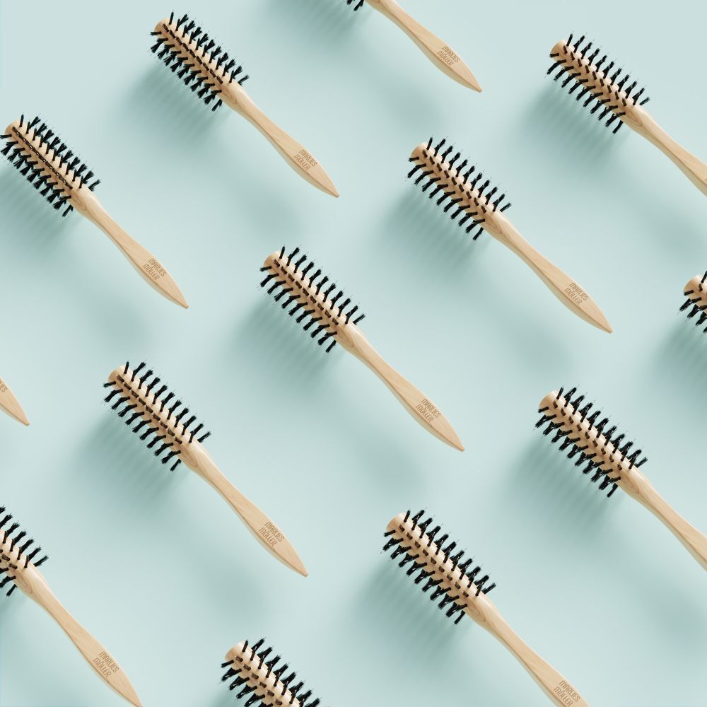 Mehrere runde Haarbürsten auf hellblauem Hintergrund. Holzgriff, schwarze Borsten. Markenschriftzug auf dem Griff.