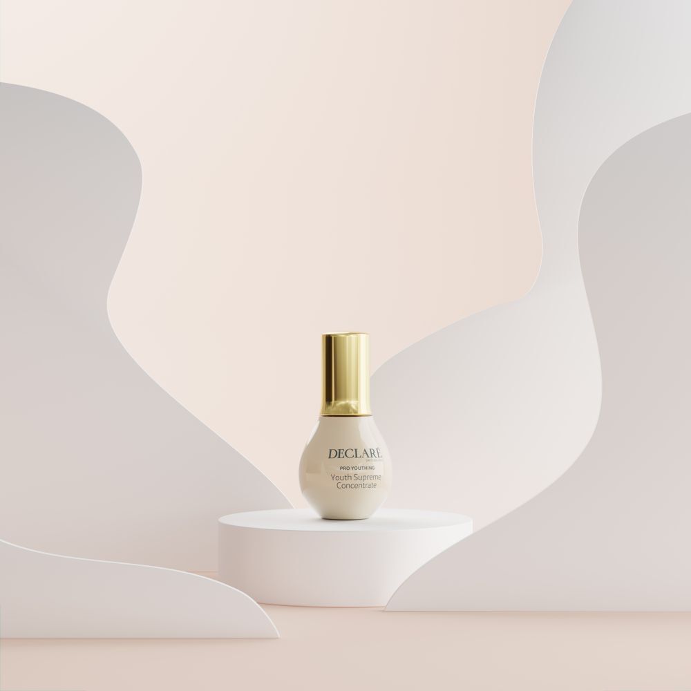 Beige Flasche mit goldenem Deckel auf weißem Podest. Hintergrund: abstrakte Formen in Beige.