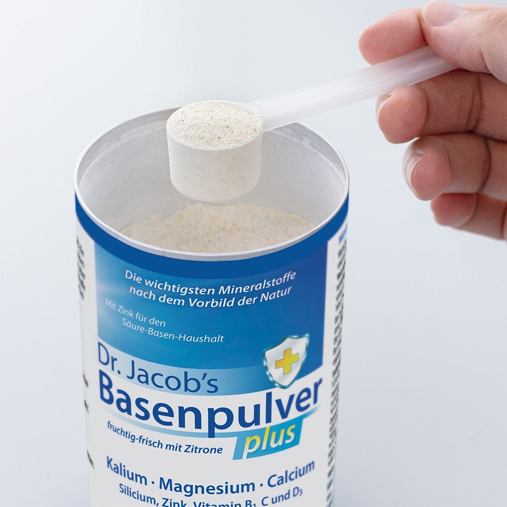 Hand hält Messlöffel mit Pulver über Dose Dr. Jacob's Basenpulver plus. Text: Basenpulver, Formule alcalinisante plus.