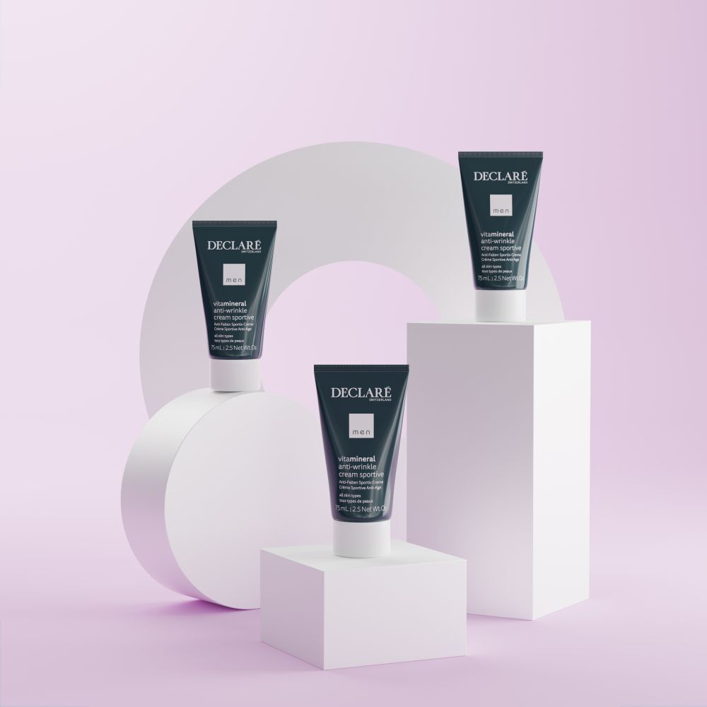 Drei Tuben Declare Anti-Falten-Creme auf weißen Podesten. Hintergrund mit geometrischen Formen in Pastelltönen.