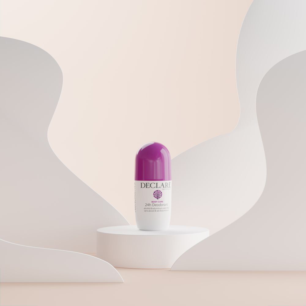 Roll-on-Deo auf Podest. Weißes Gehäuse, lila Kappe. DECLARÉ, 24h Deodorant. Hintergrund: weiße, geschwungene Formen.