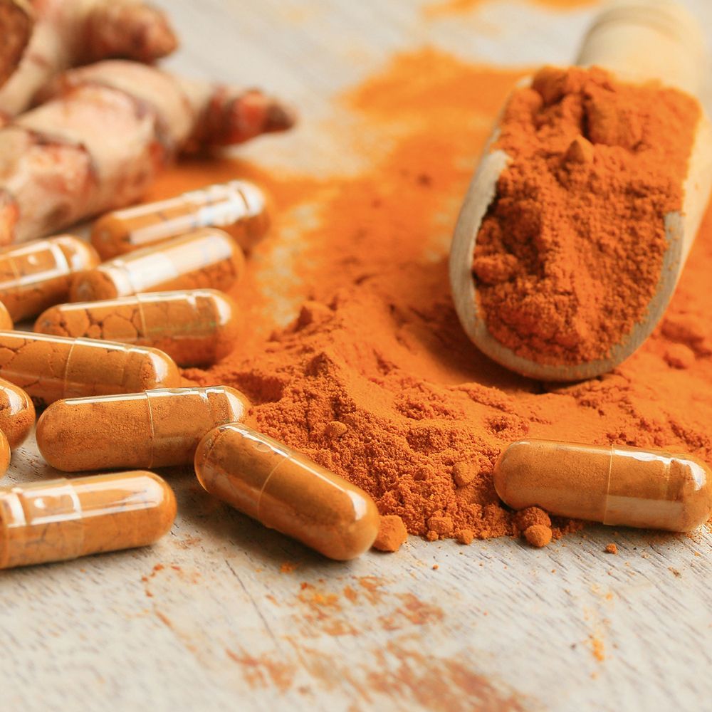 Gélules, poudre de curcuma et gingembre. Gélules oranges. Poudre dans un bol en bois.