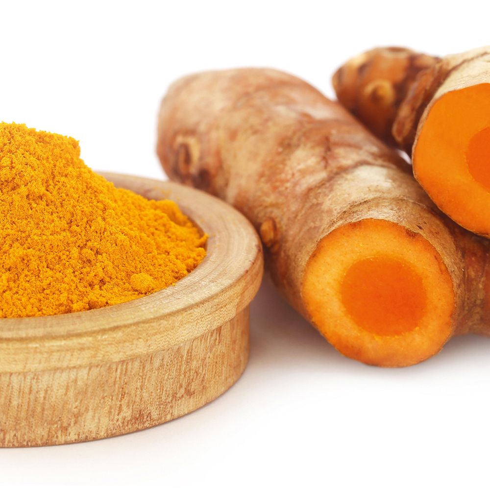 Poudre de curcuma dans un bol en bois, gingembre et morceaux de curcuma. Fond blanc.