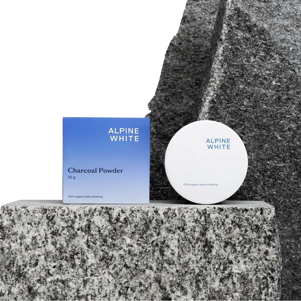 Blau-weiße Schachtel und Dose auf Steinen. Text: ALPINE WHITE, Charcoal Powder, 30 g.