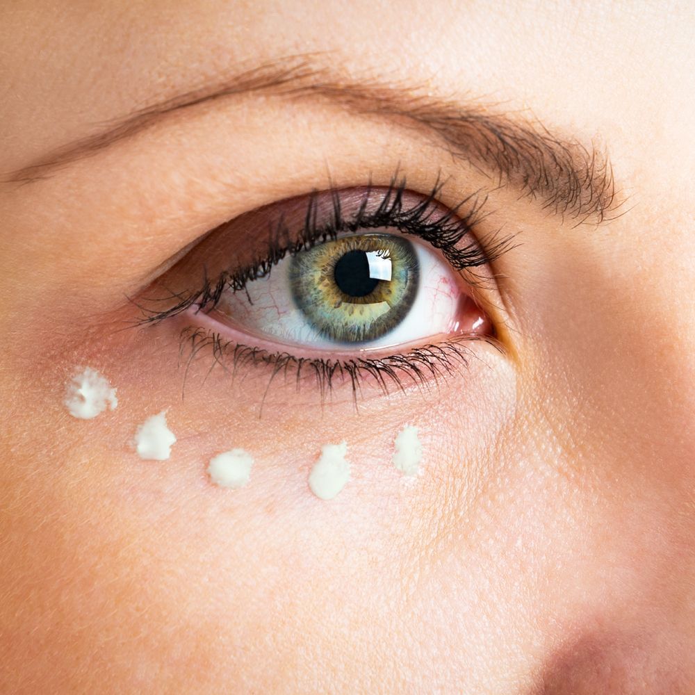 Nahaufnahme eines Auges mit Creme-Punkten unter dem Auge.