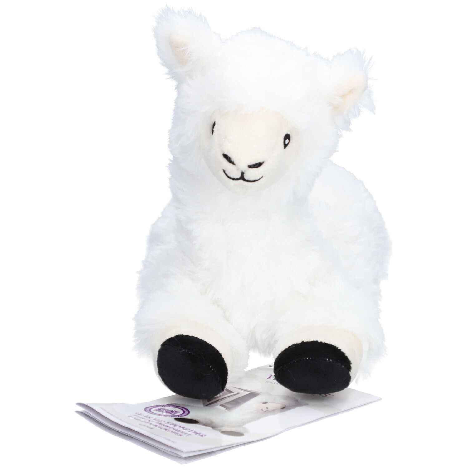 Peluche lama blanc, pieds noirs. Il est assis sur un dépliant. Oreilles, yeux et bouche sont visibles.