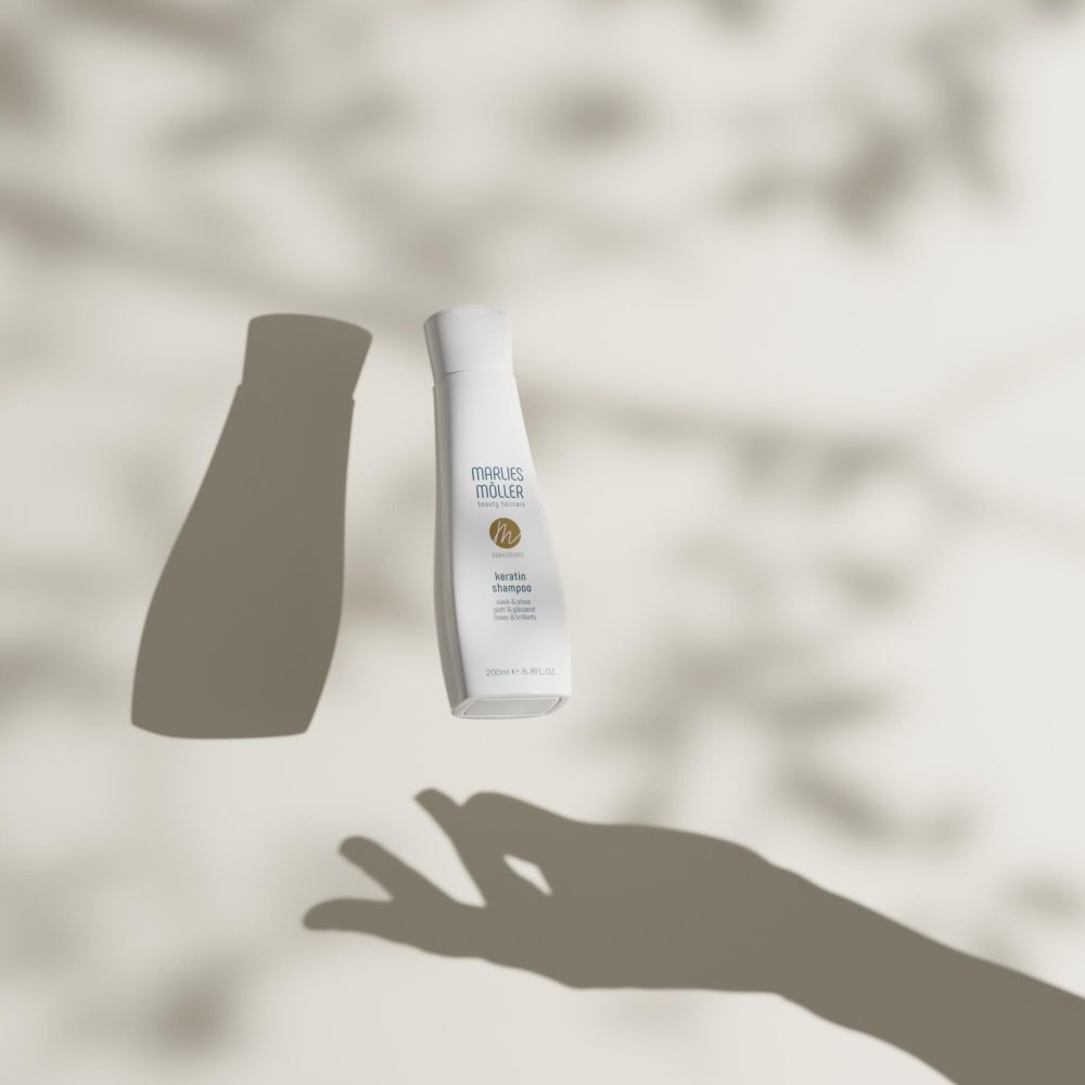 Marlies Möller Keratin Shampoo-Flasche in der Luft. Schatten einer Hand und Blätter.