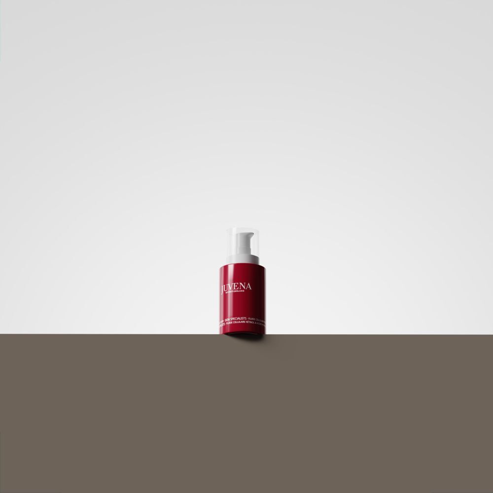 Rote Flasche mit weißem Pumpkopf. Aufschrift: Juvena. Produkt steht auf braunem Untergrund vor weißem Hintergrund.