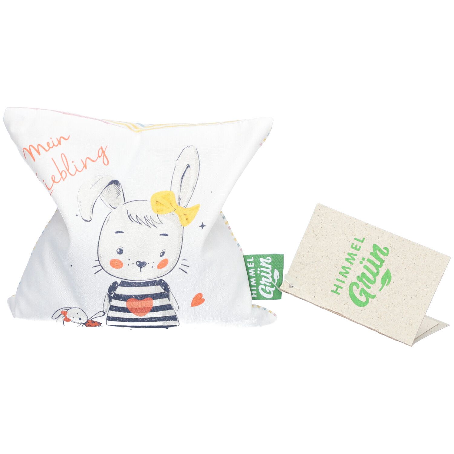 Weißes Kissen mit Hasenmotiv und Aufdruck "Mein Liebling". Grünem Etikett und Pappschild mit "Himmel Grün" Logo.