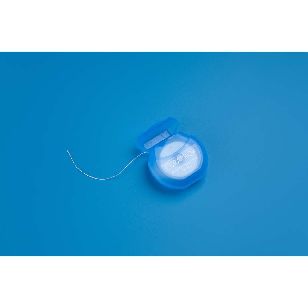 Blaue Zahnseide-Spule mit herausgezogenem Faden. Auf blauem Hintergrund.