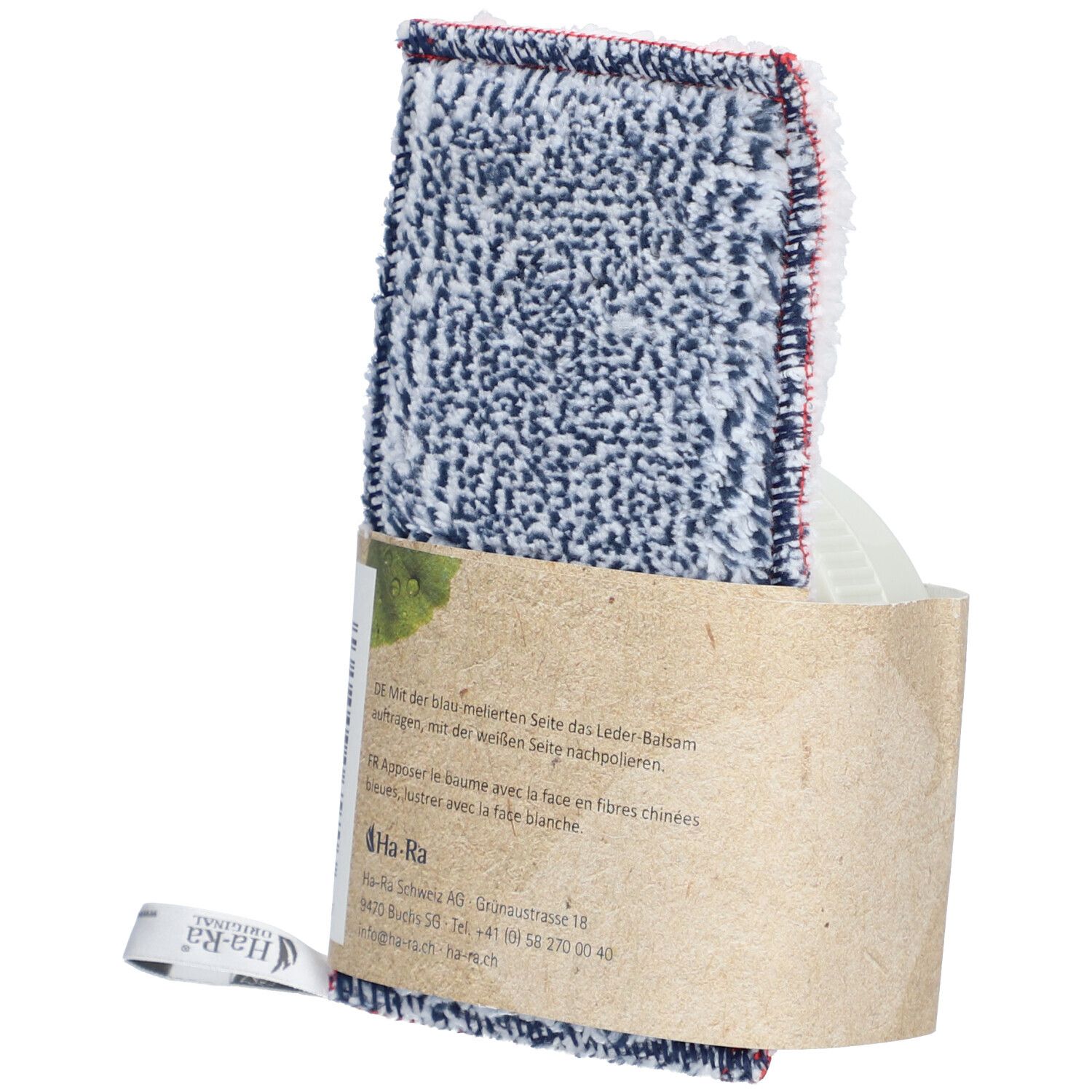 Pflegetuch mit Lederbalsam-Verpackung. Tuch mit blau-weißem Muster und rotem Rand. Verpackung aus braunem Papier. Text auf der Verpackung.