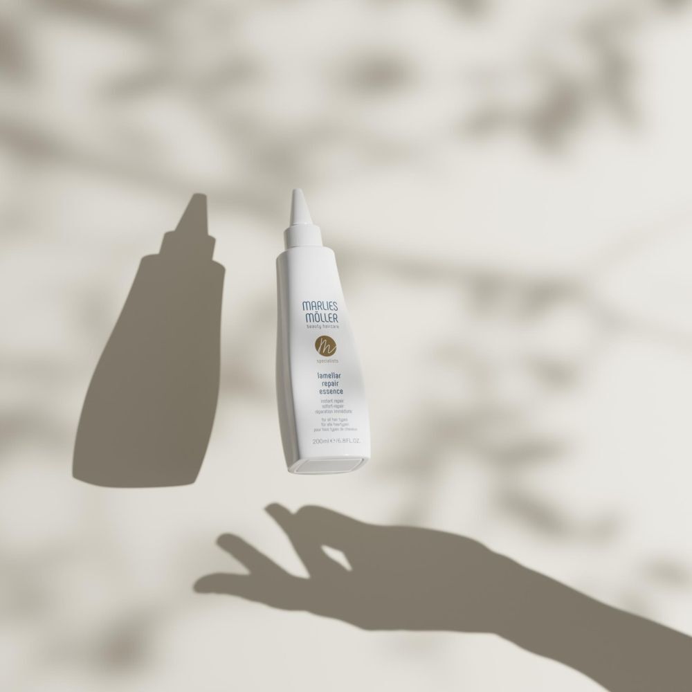 Weiße Flasche mit Spitze, Marlies Möller, Lamellar Repair Essence, mit Schatten. Hand-Silhouette im Hintergrund.