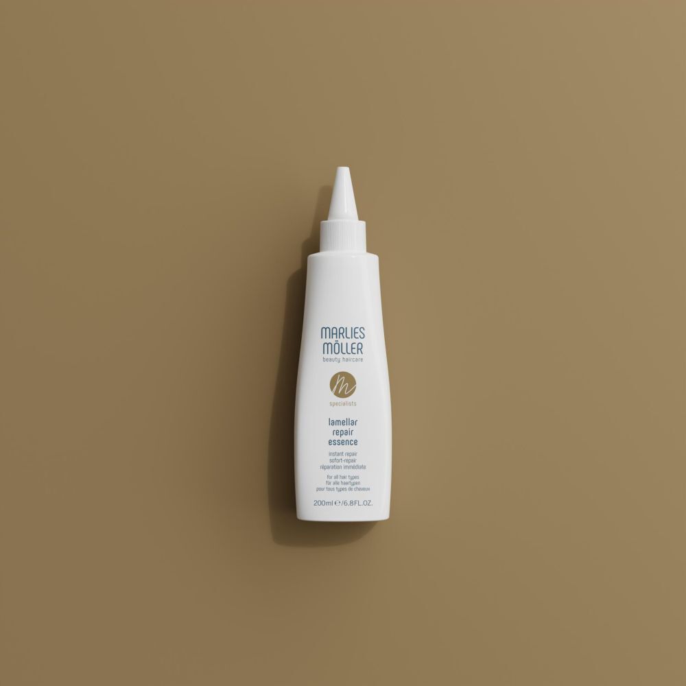 Weiße Flasche mit Spitze, Marlies Möller, Lamellar Repair Essence, auf braunem Hintergrund. Draufsicht.