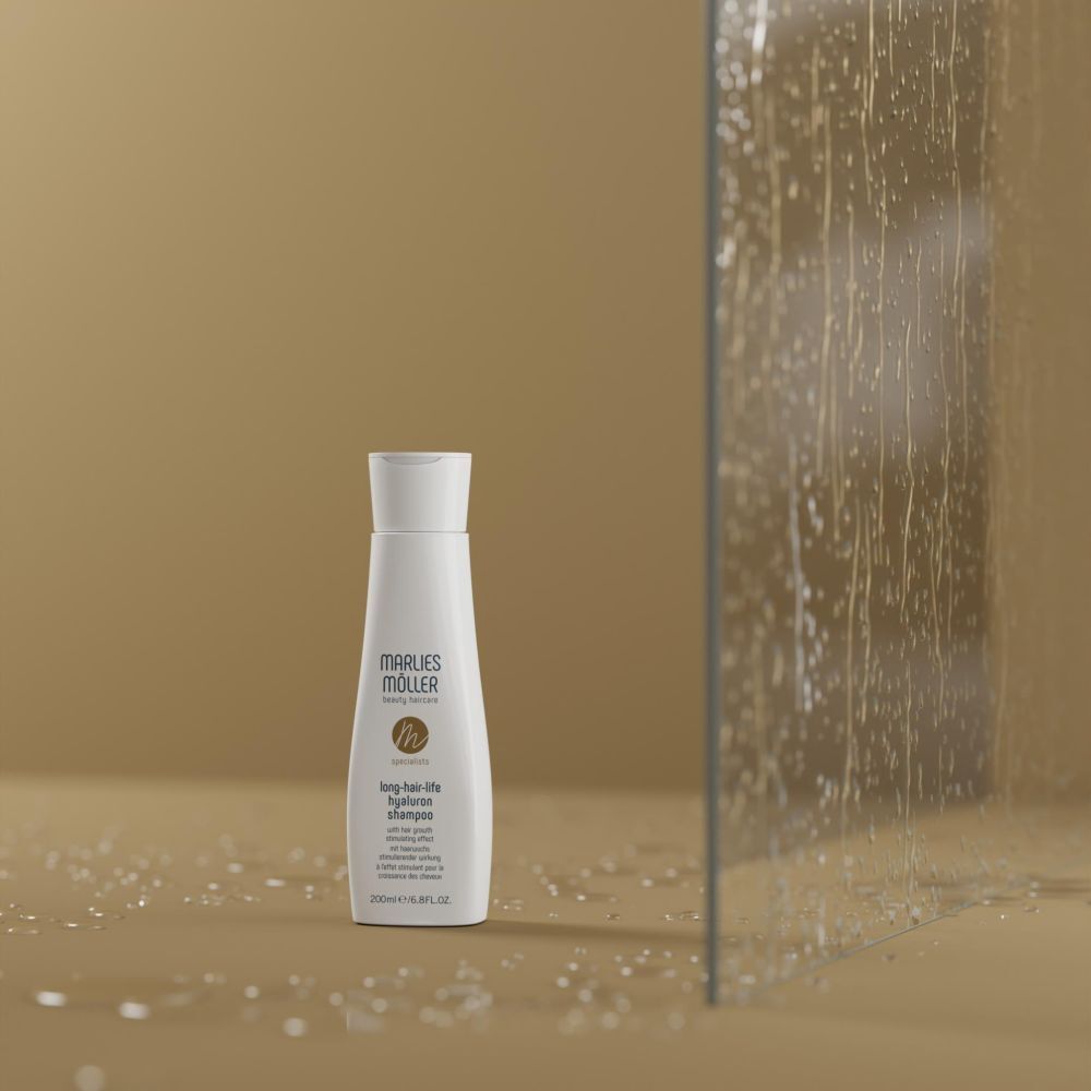 Weißes Shampoo-Fläschchen mit weißem Deckel. Aufschrift: Marlies Möller, Lang-Haar-Life Hyaluron Shampoo. Hintergrund: Glaswand.