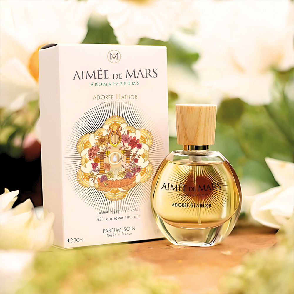 Produktverpackung und Flakon. Verpackung: AIMÉE DE MARS, ADORÉE HATHOR. Flakon: rund, Glas, Holzverschluss.