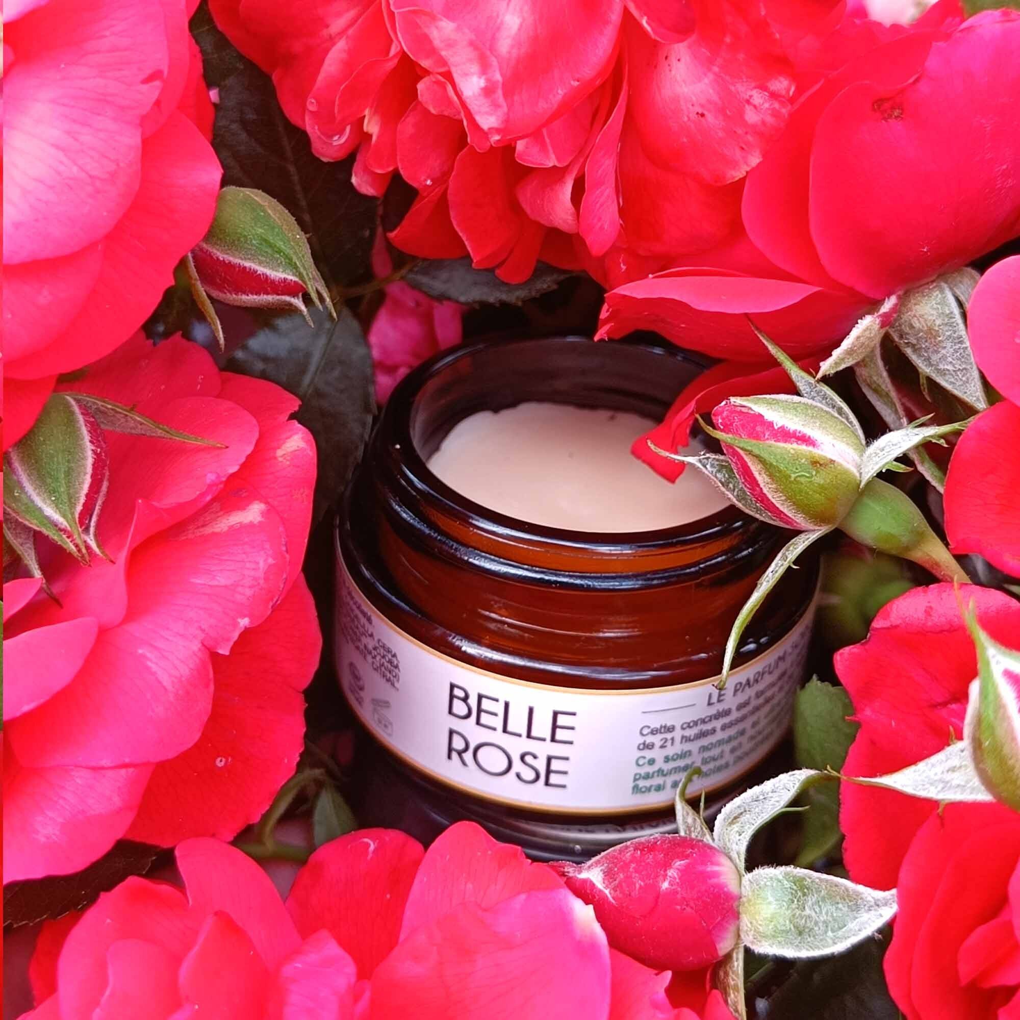 Kleines Glas mit "Belle Rose"-Etikett, umgeben von roten Rosenblüten. Der Inhalt des Glases ist sichtbar.