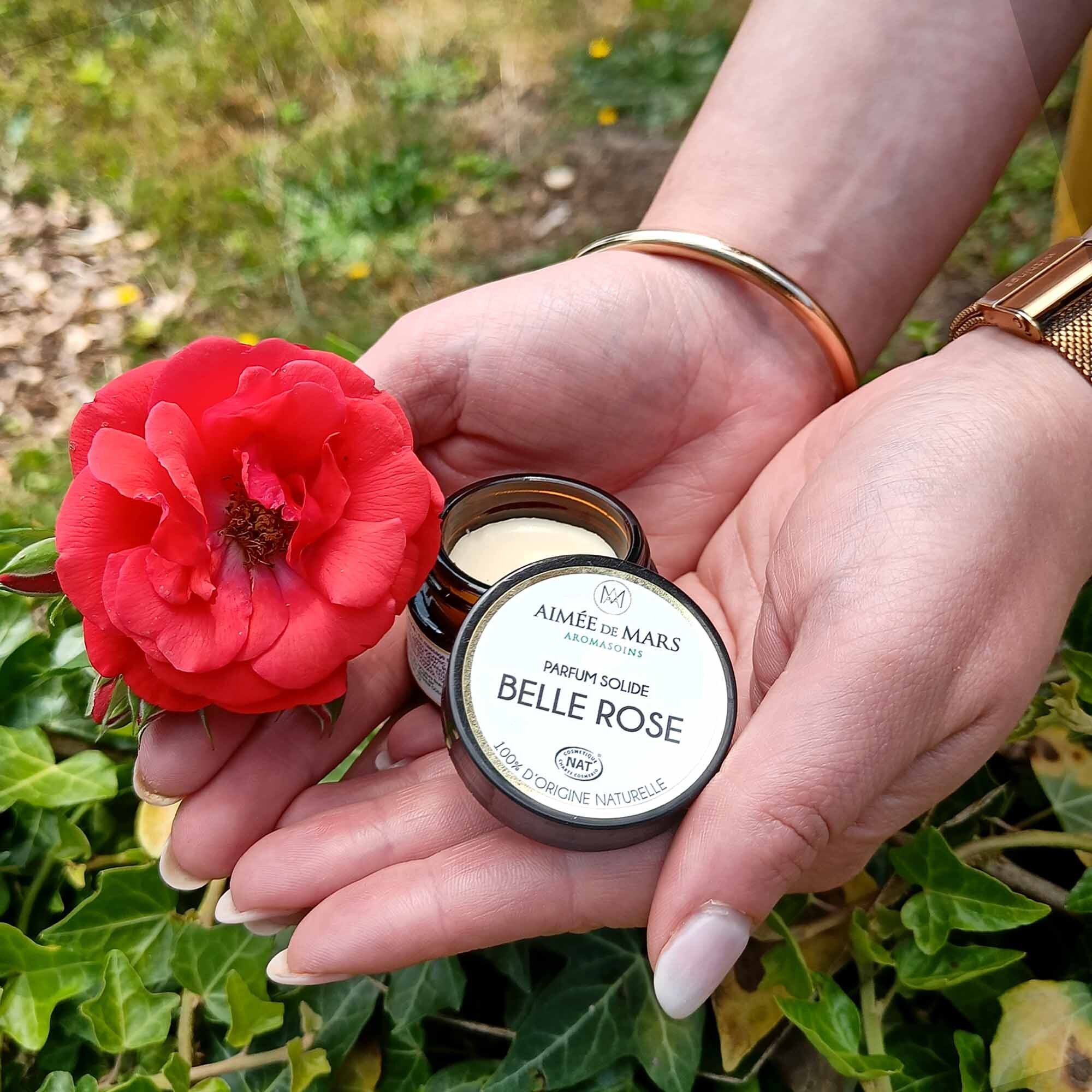 Hände halten ein offenes Glas mit "Belle Rose" und eine rote Rose. Auf dem Glas steht "Parfum Solide".