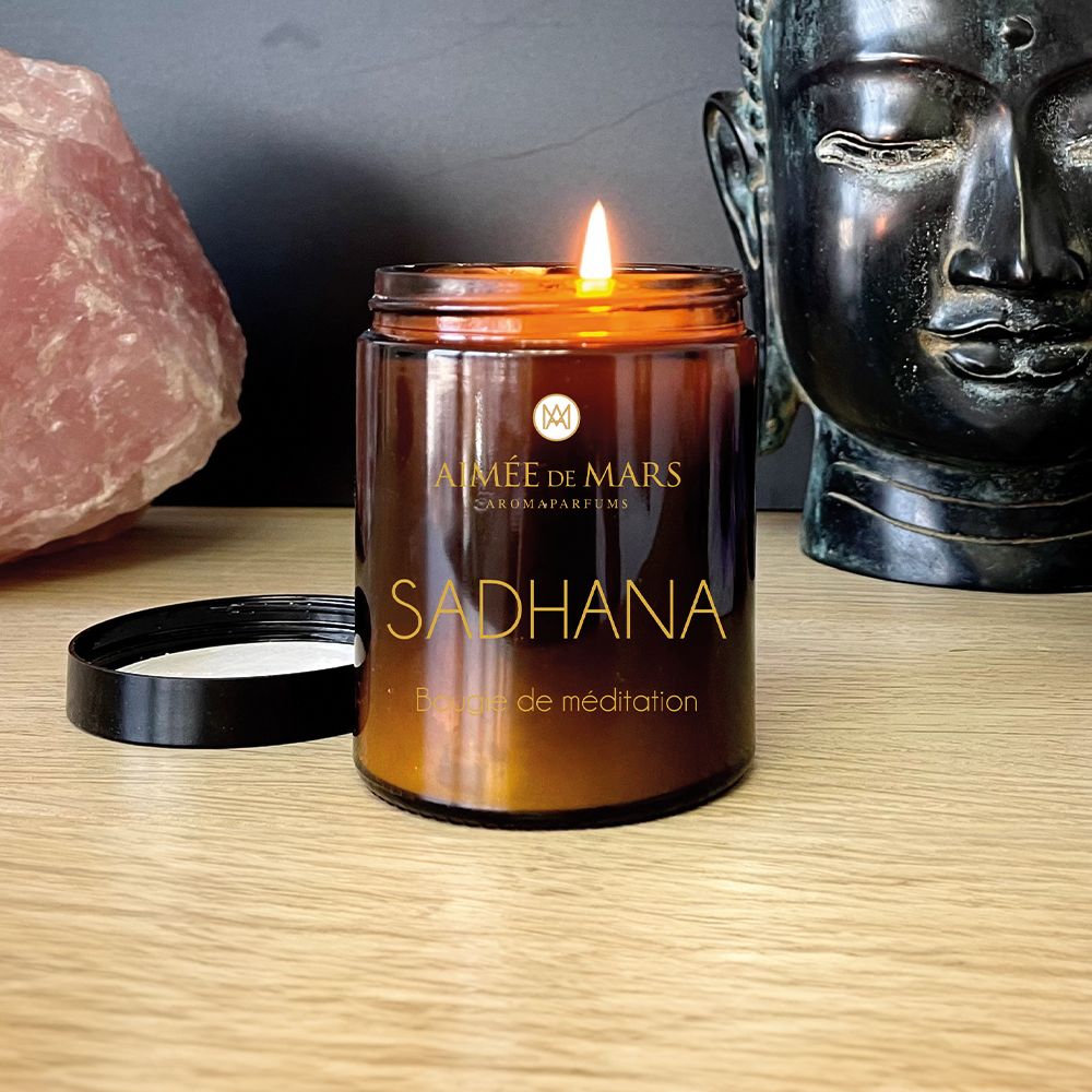Brennende braune Kerze mit schwarzem Deckel. Aufschrift: AIMÉE DE MARS, SADHANA, Bougie de méditation.