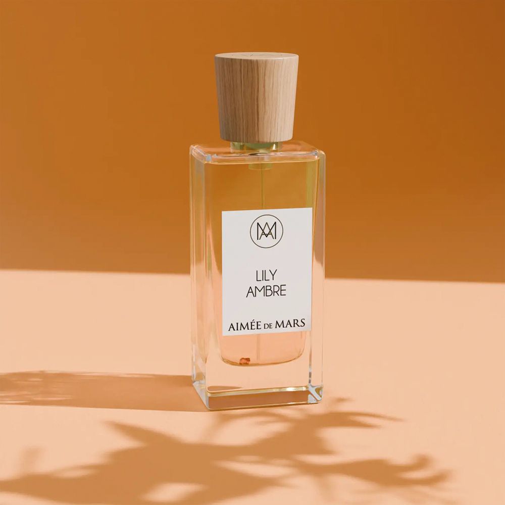 Parfümflakon mit Holzverschluss. Aufschrift: LILY AMBRE, AIMÉE DE MARS. Rechteckige Glasflasche mit goldener Flüssigkeit.