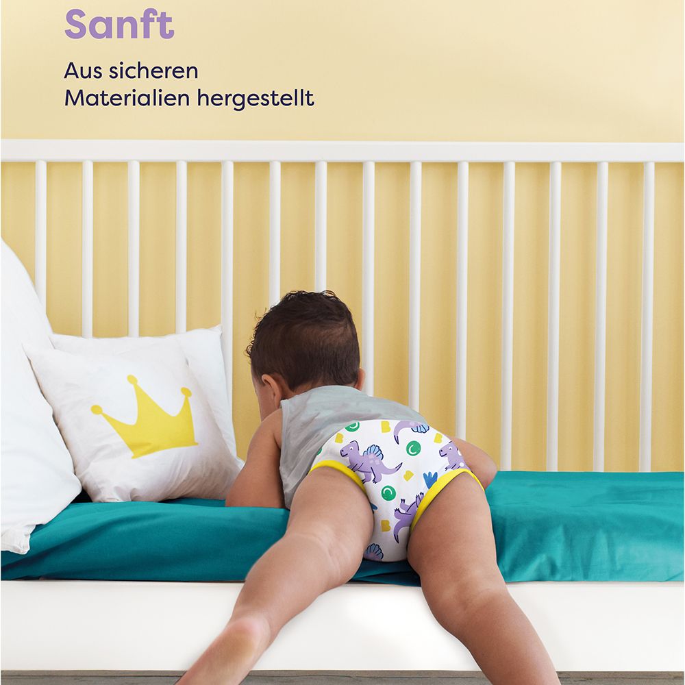 Enfant avec culotte d'apprentissage sur un lit. Texte : Doux. Fabriqué avec des matériaux sûrs. Marque : Bambino Mio.