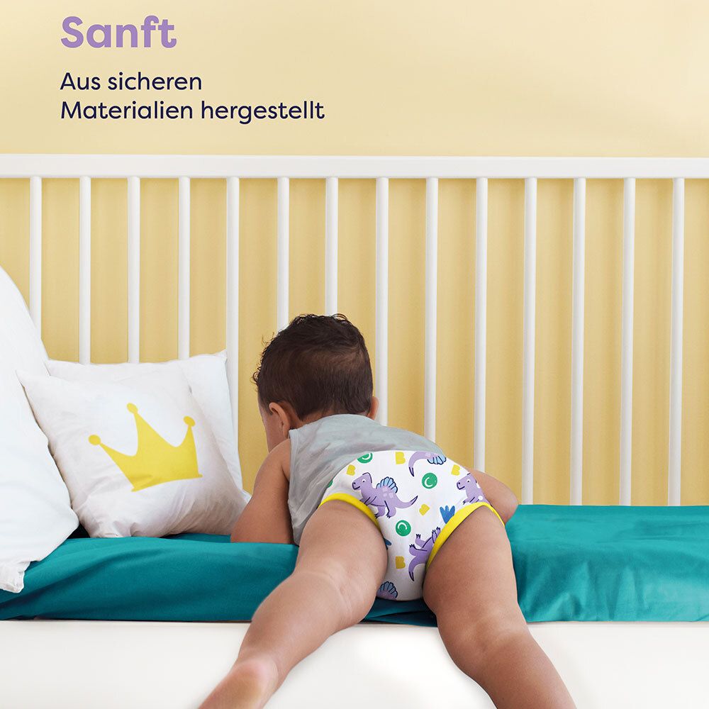 Kind liegt auf dem Bett. Lernhöschen mit Dinosaurier-Muster. Text: Sanft. Aus sicheren Materialien.