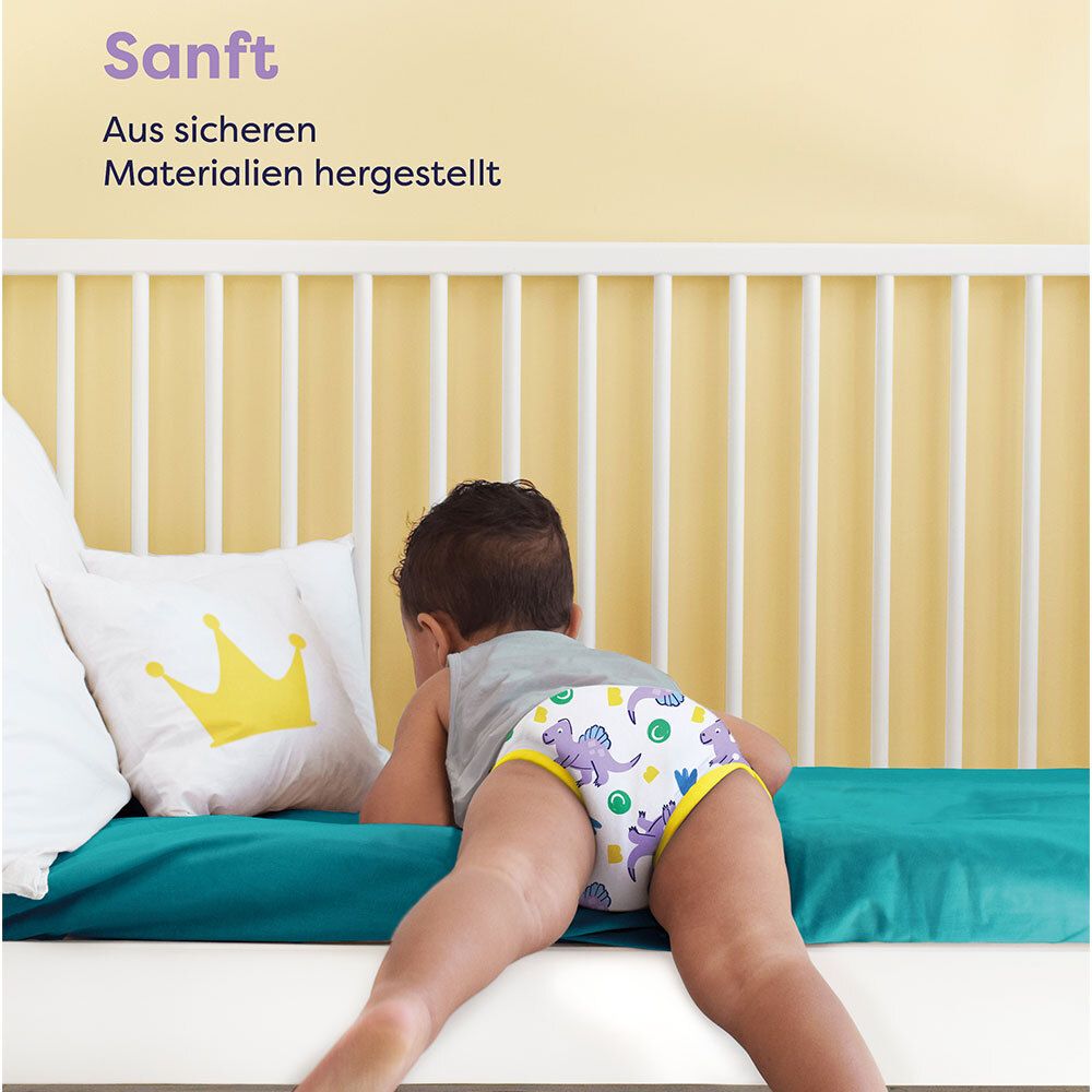 Kind liegt auf dem Bauch. Lernhöschen mit Dinosaurier-Motiv. Gelber Bund. Text: Sanft. Aus sicheren Materialien hergestellt.