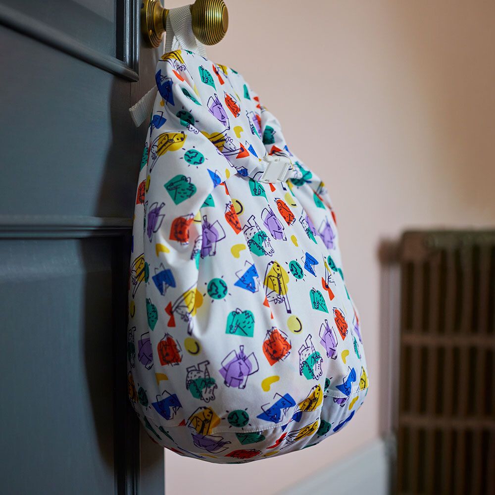 Sac à couches blanc avec motif coloré, fixé à une porte. Avec cordon de serrage et fermeture blanche.