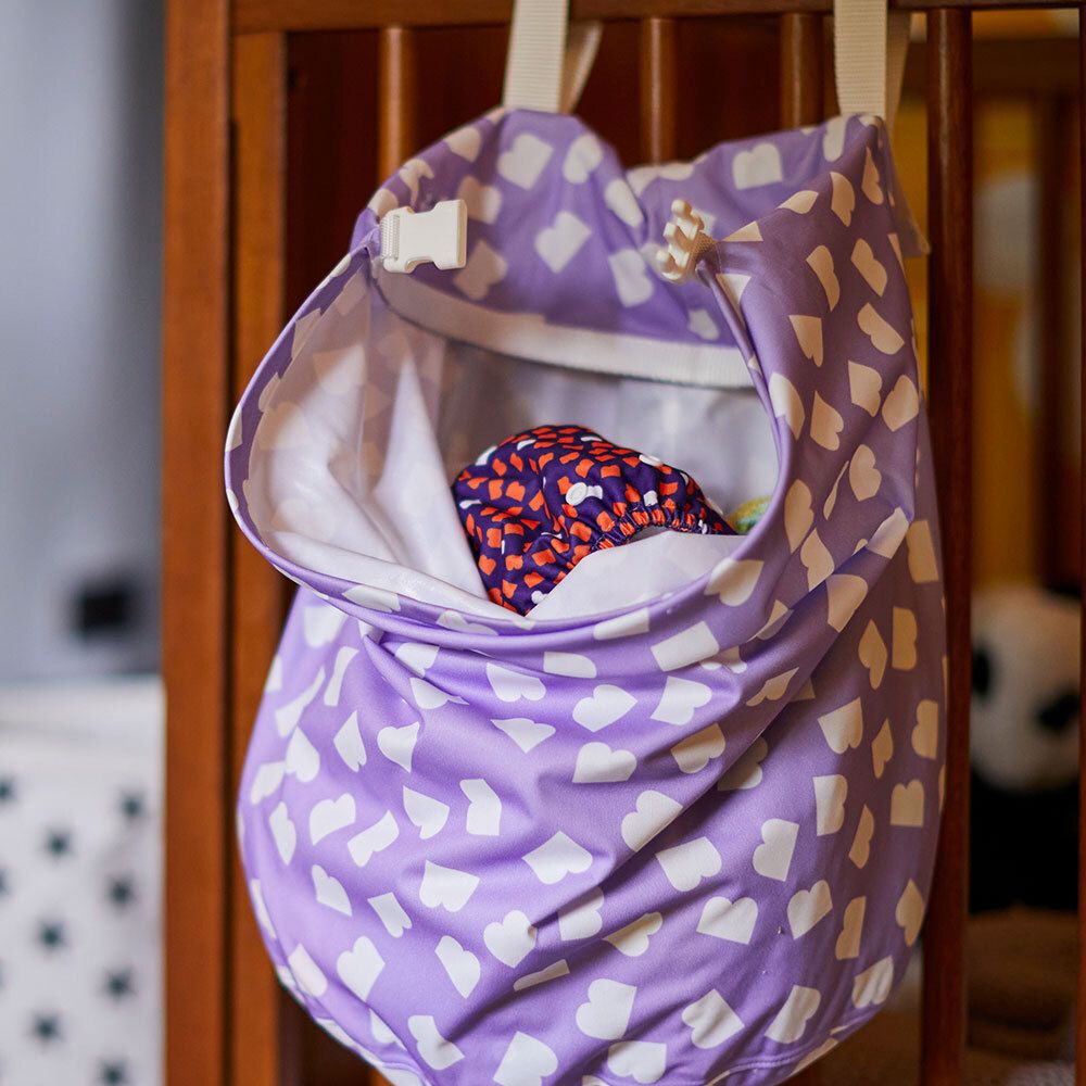 Sac à couches violet avec des cœurs blancs, fixé à un lit bébé. Intérieur avec couche. Avec fermeture blanche.