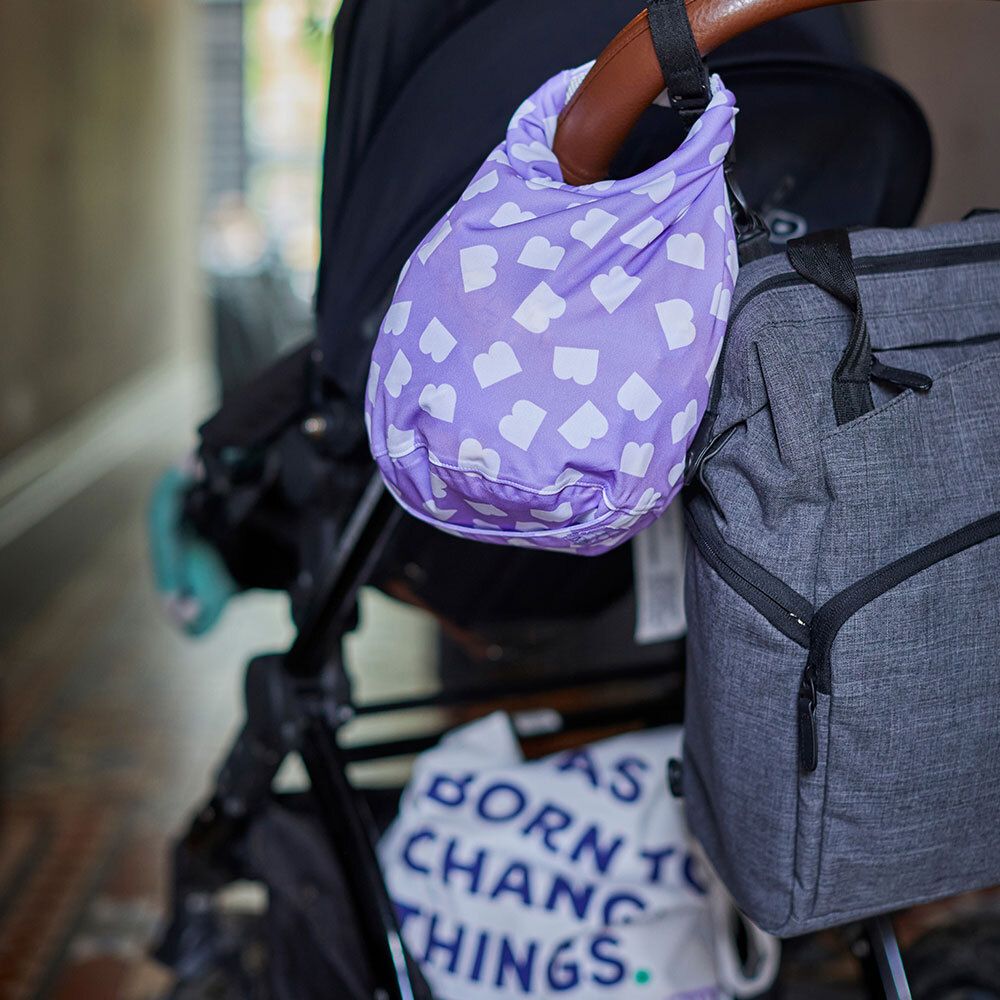 Paarse stoffen tas met wit hartpatroon bevestigd aan een kinderwagen.