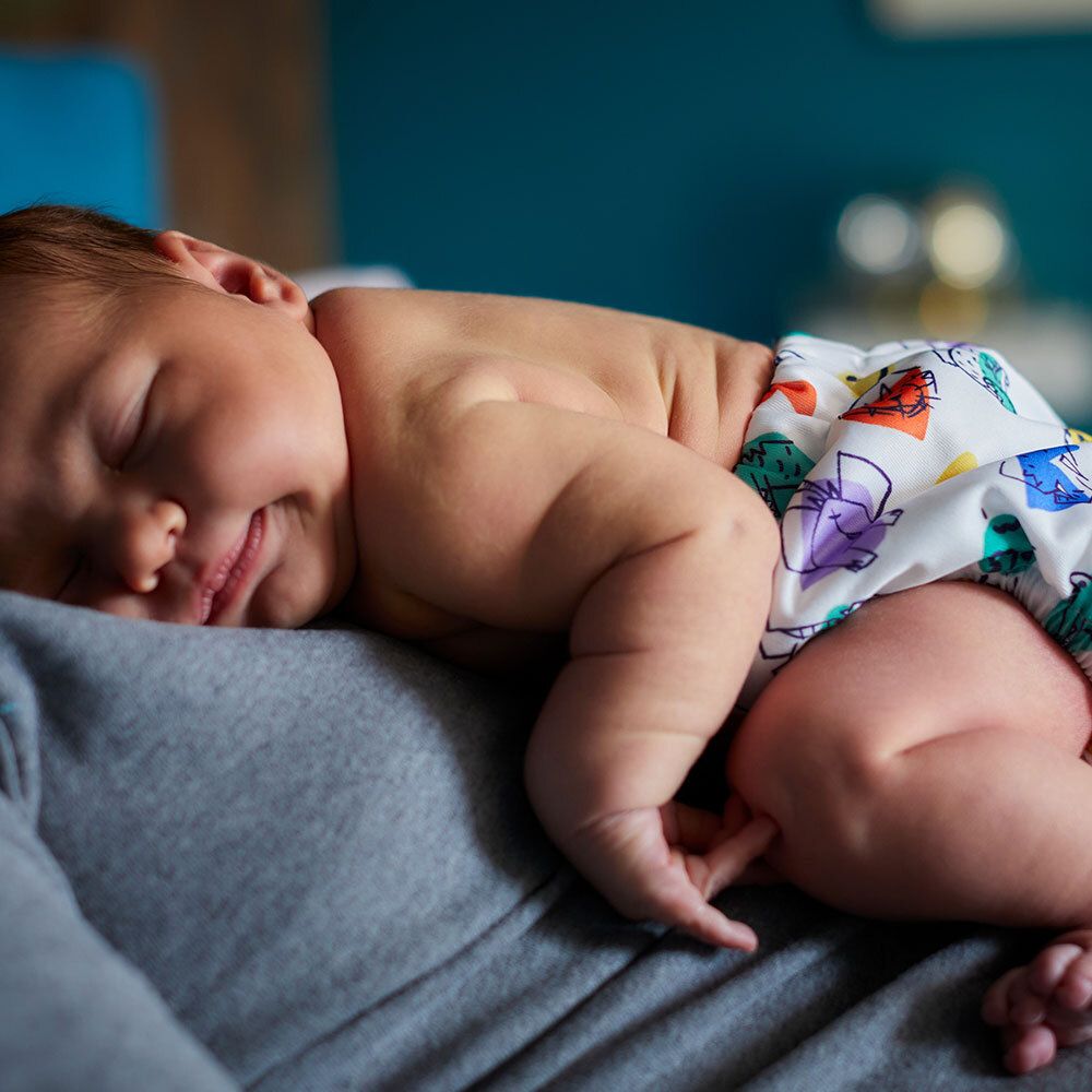 Baby liegt auf dem Bauch, trägt eine Stoffwindel mit bunten Mustern.