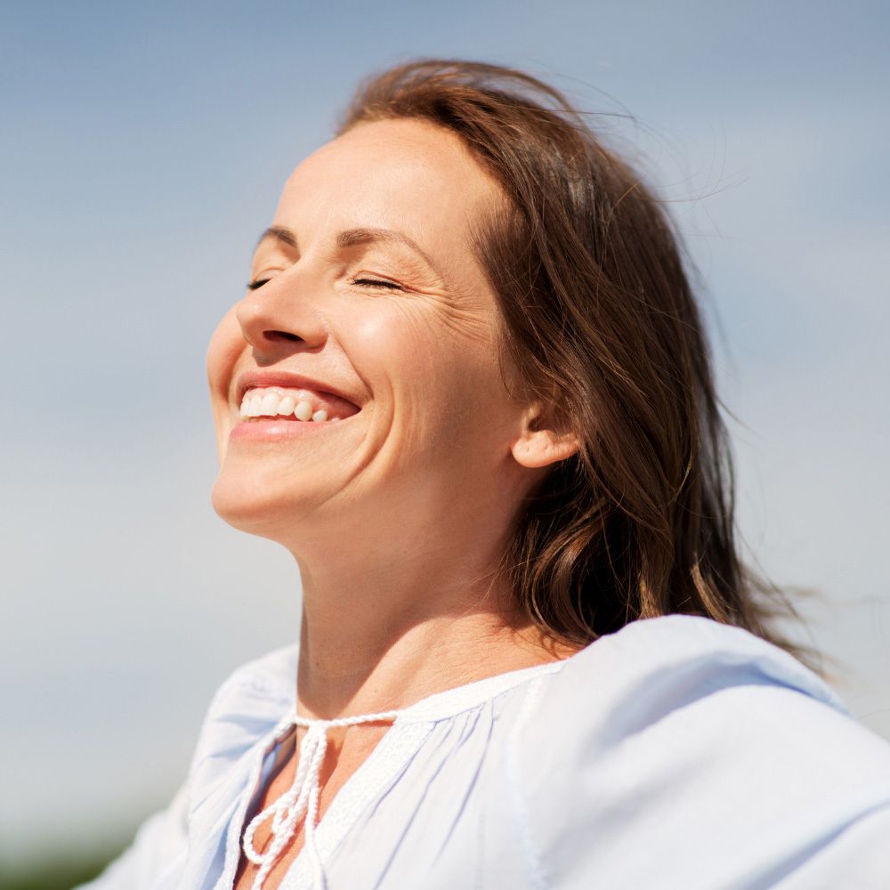Lächelnde Frau im Freien. Sie trägt ein hellblaues Oberteil. Sonnenschein.