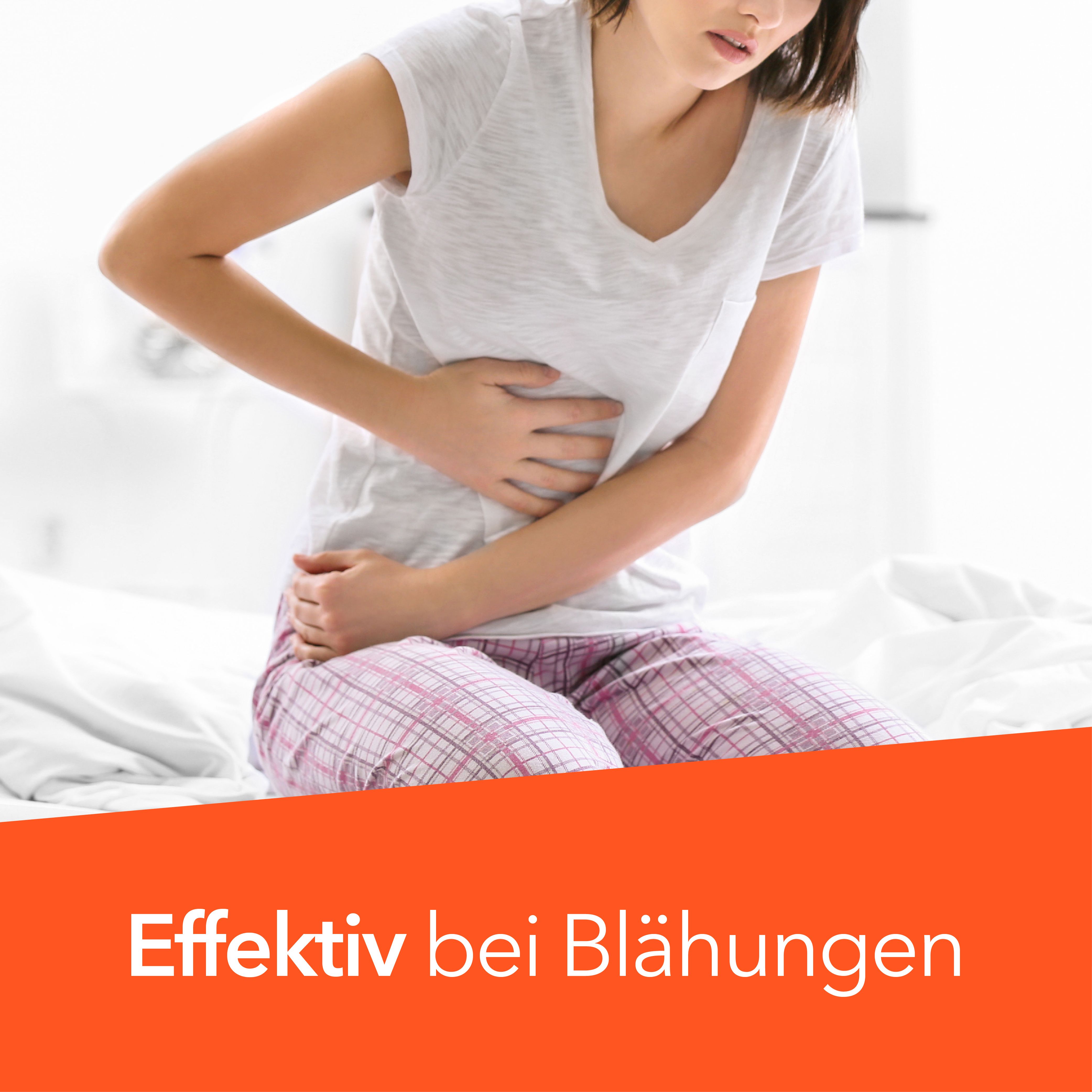 Frau sitzt auf Bett, hält Bauch. Orangefarbener Balken mit Text: Effektiv bei Blähungen.