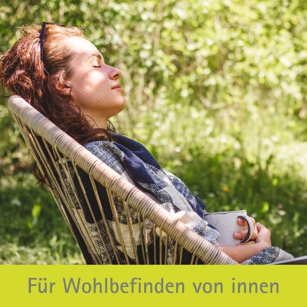 Eine Frau sitzt entspannt in einem Stuhl im Freien. Sie hält eine Tasse.