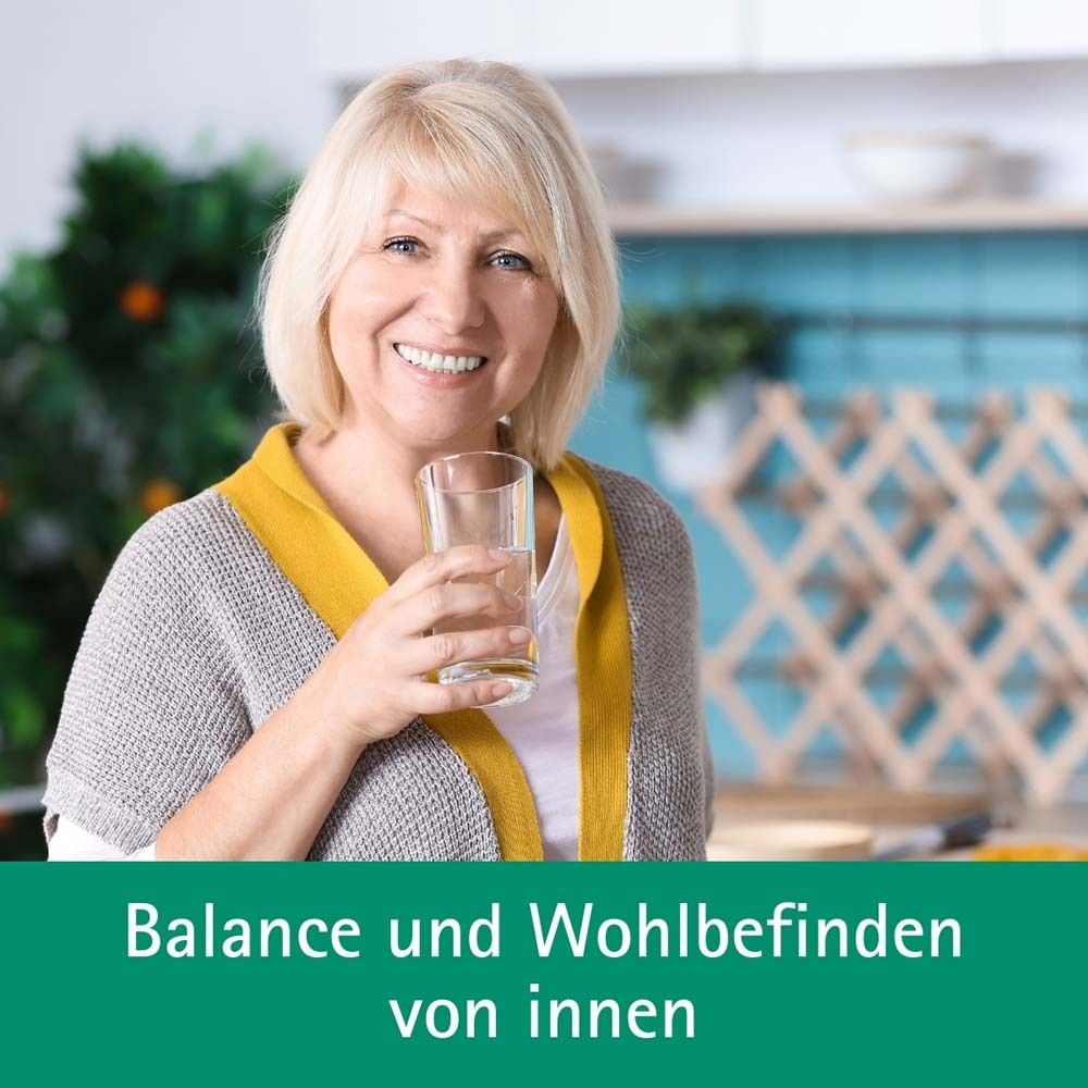 Ältere Frau lächelt. Sie hält ein Glas Wasser. Text: Balance und Wohlbefinden von innen.
