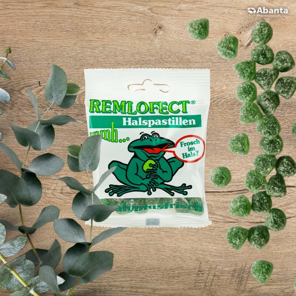 Packung REMLOFECT Halspastillen auf Holz. Grün-weiße Verpackung mit Frosch-Illustration. Text: Eukalyptusfrisch.
