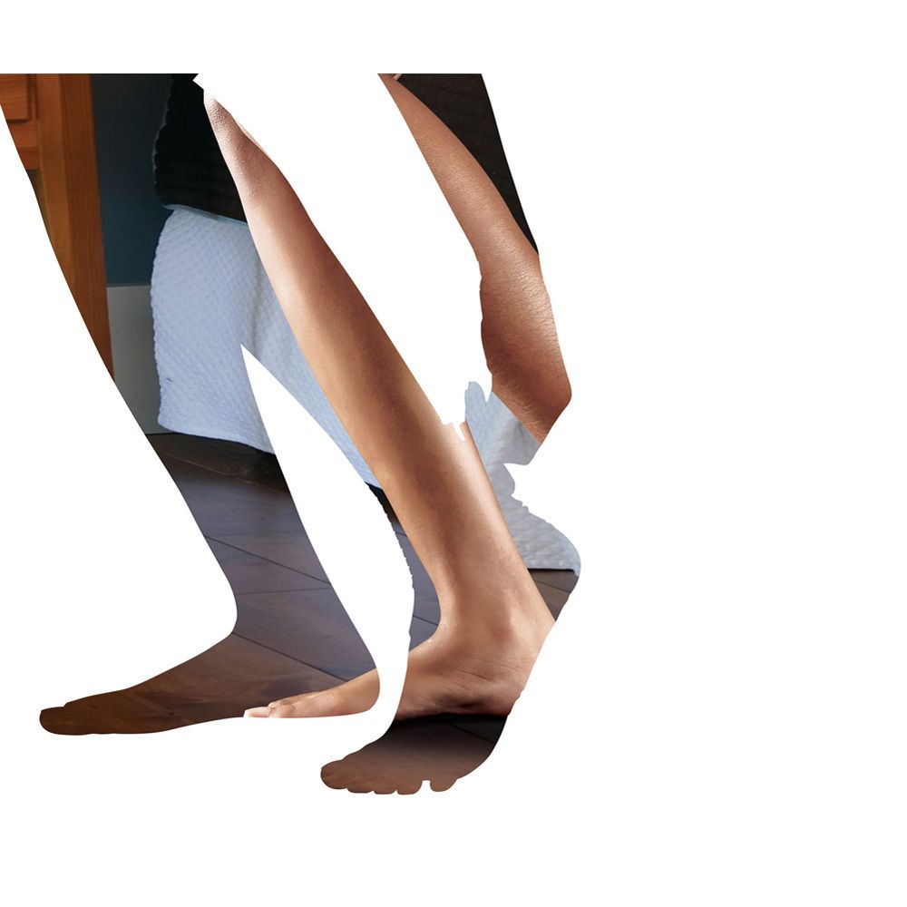 Beine und Füße. Eine Person trägt eine weiße Bandage am Fuß. Holzfußboden im Hintergrund.