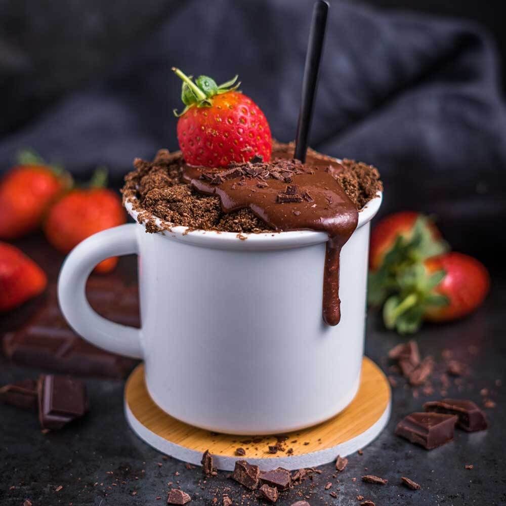 Weißer Becher mit Schokoladenkuchen und Erdbeere. Schokoladensauce läuft herunter. Erdbeeren und Schokoladenstücke.