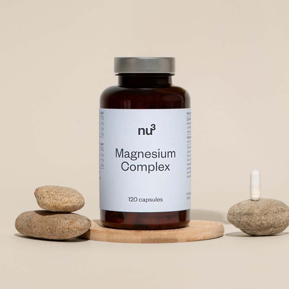 Braune Flasche mit weißem Etikett. Aufschrift: Magnesium Complex, 120 Kapseln. Dekoration: Steine und Holz.