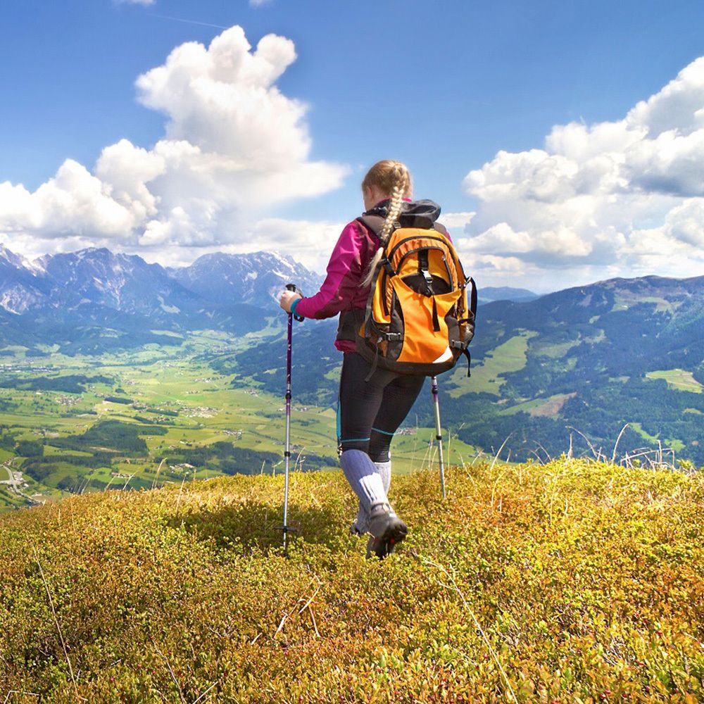 Personne avec sac à dos et bâtons de randonnée sur une colline. Paysage de montagne en arrière-plan.