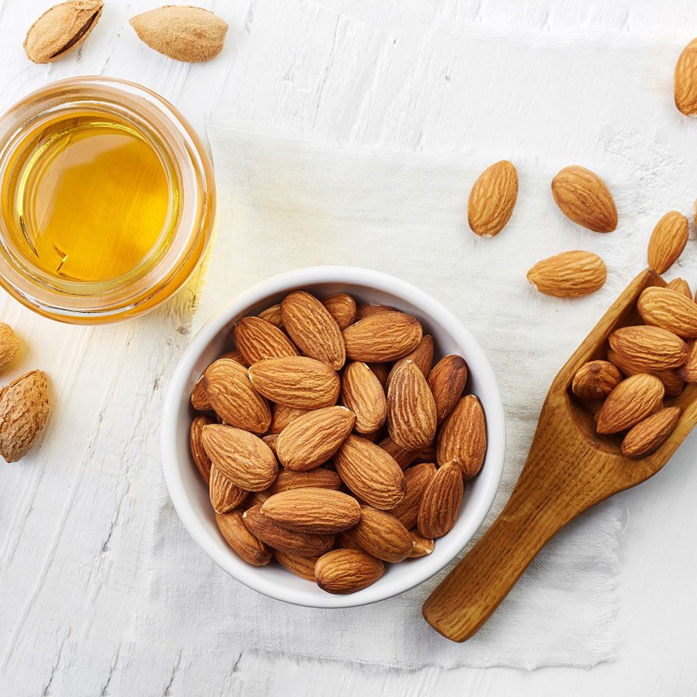 Verre d'huile et bol d'amandes. Pelle en bois avec des amandes. Sur fond blanc. Amandes en gros plan.