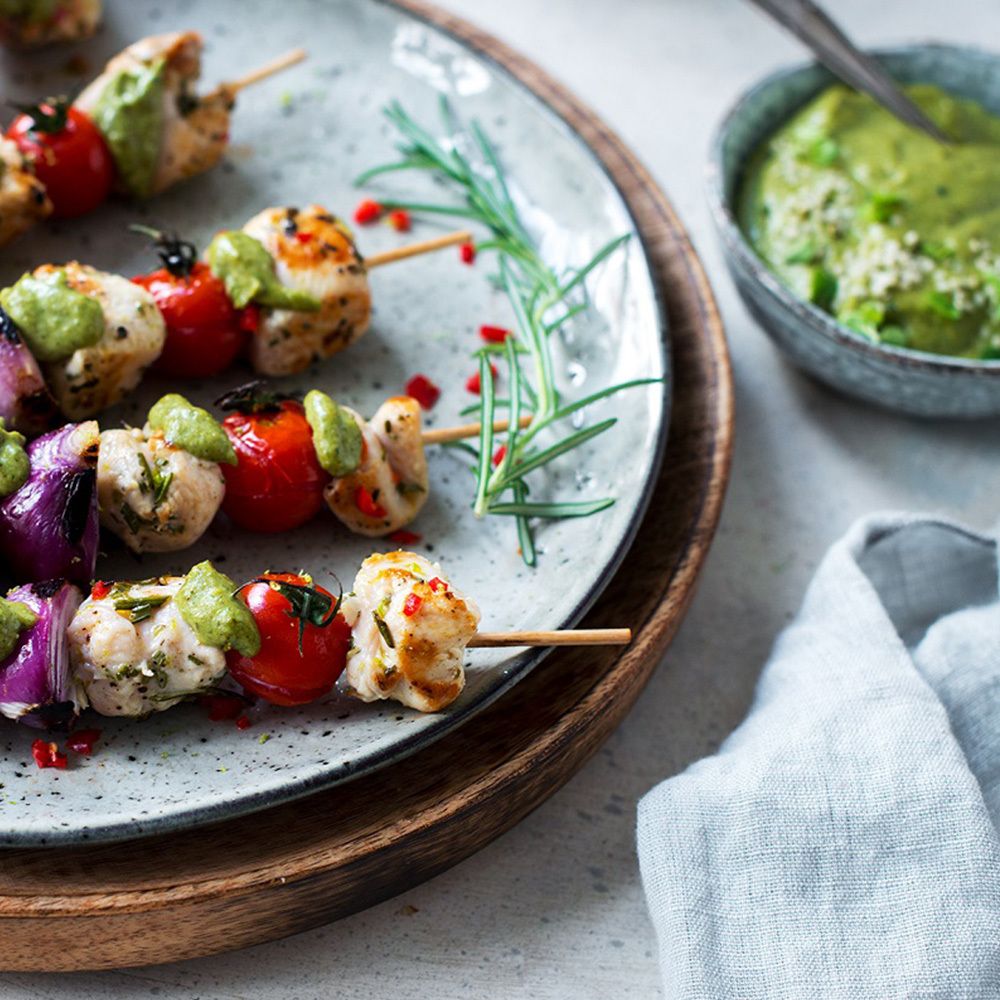 Hühnchen-Spieße mit Tomaten und Soße. Auf einem Teller mit Kräutern. Auf einem Holztablett.