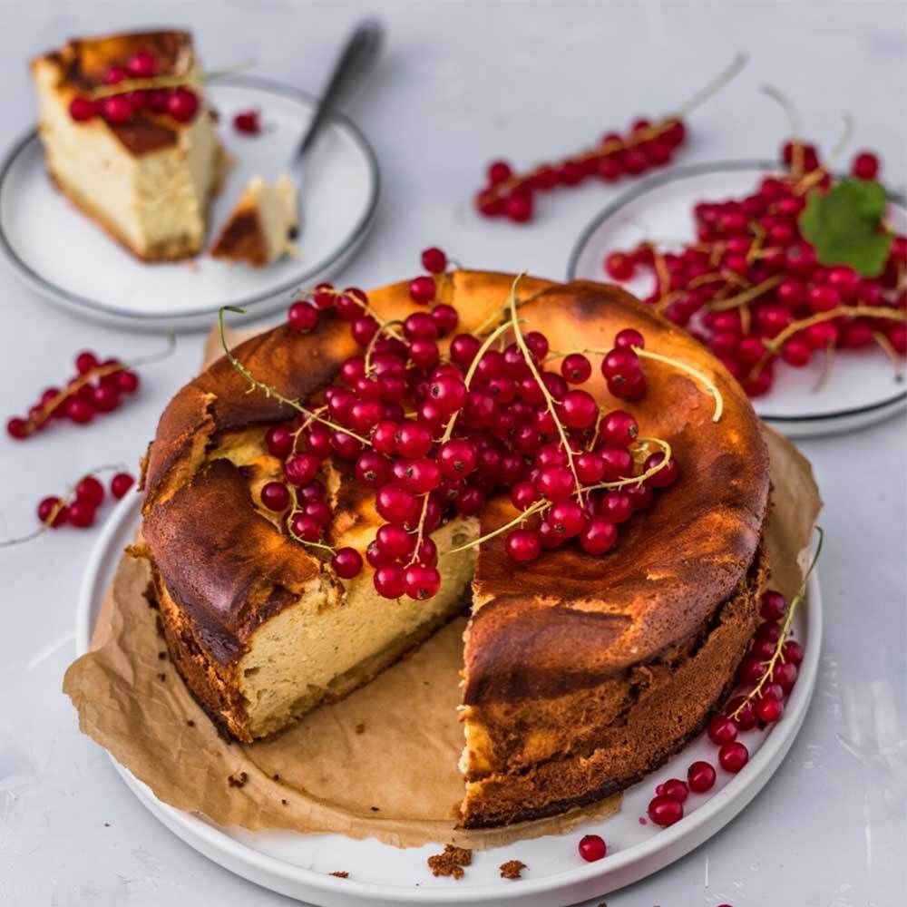 Käsekuchen mit roten Johannisbeeren. Auf einem Teller, daneben weitere Teller mit Beeren.