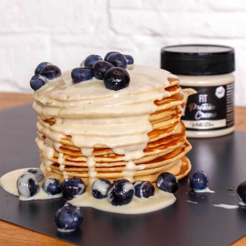 Crêpes avec nu3 Fit Protein Creme, White-Choc et myrtilles. Crème sur crêpes et à côté. Fond noir.
