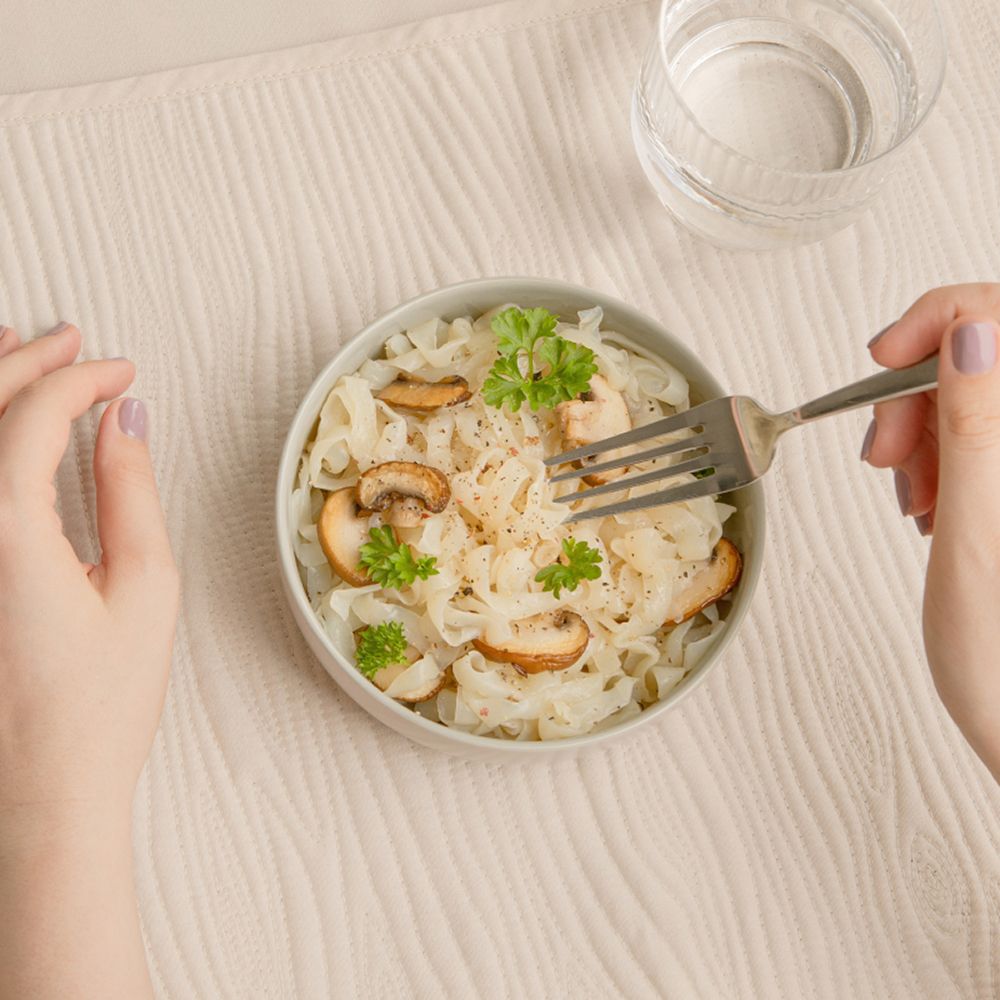 Eine Schüssel Konjak-Tagliatelle mit Pilzen und Petersilie, von oben fotografiert, mit einer Gabel.