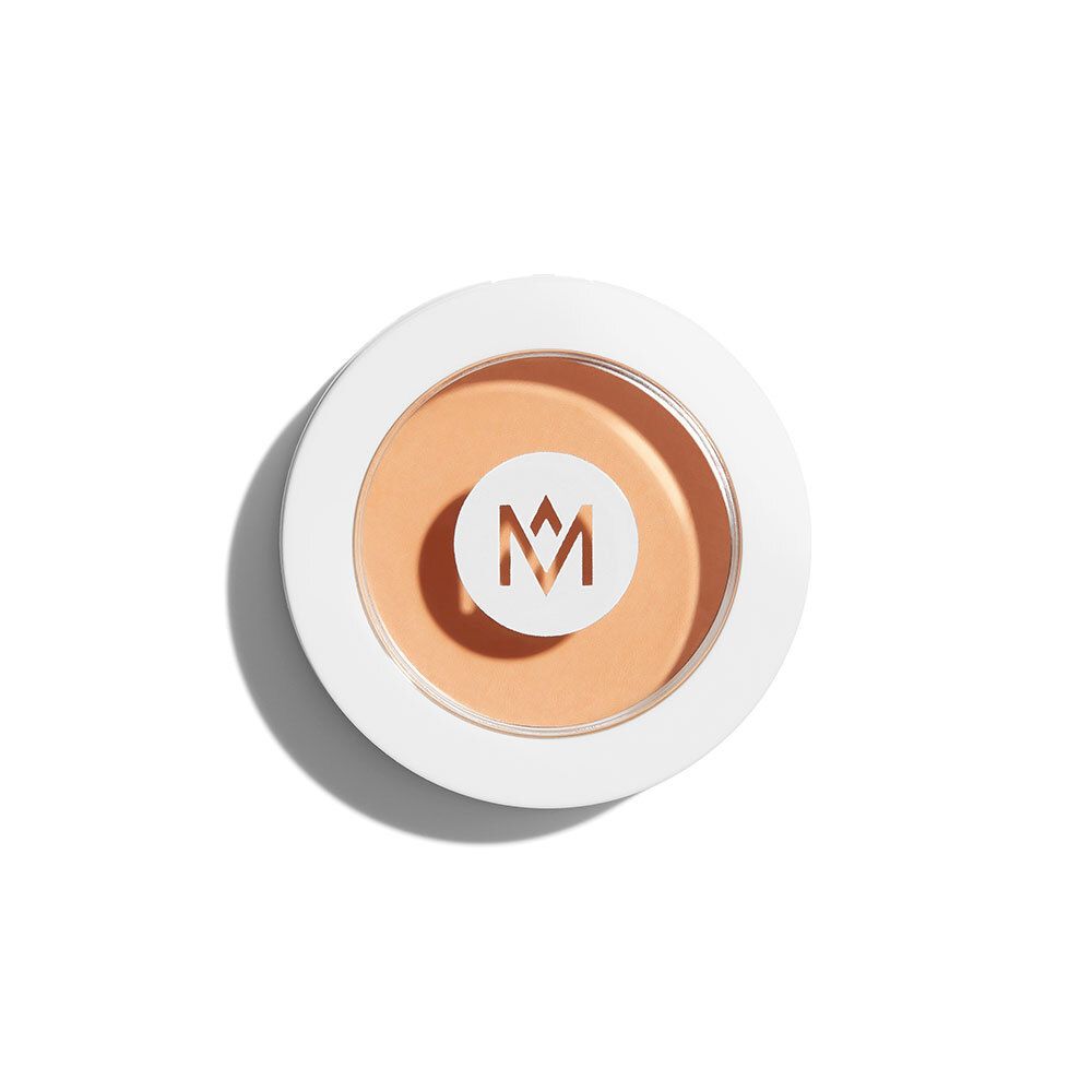 Runder Concealer-Behälter, weiß mit hellbraunem Inhalt. Logo 'M' in der Mitte.